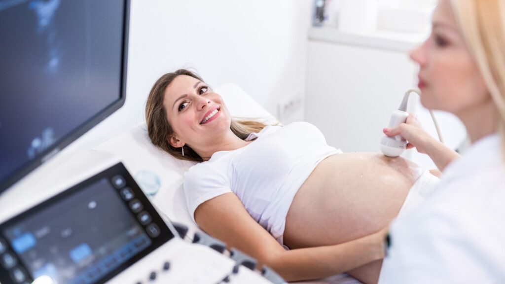 Schwangere Frau erhält eine Bauchultraschalluntersuchung durch eine medizinische Fachkraft in einer Klinik, symbolisiert Schwangerschaftsvorsorge und pränatale Betreuung.