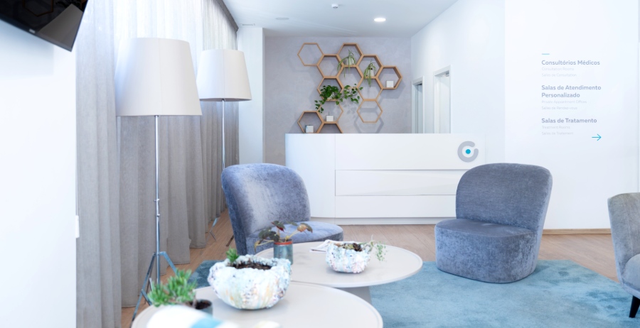Heller, freundlich gestalteter Wartebereich der Ferticentro Kinderwunschklinik in Coimbra mit bequemen grauen Sesseln, weißem Empfangstresen und dekorativen Wandelementen.