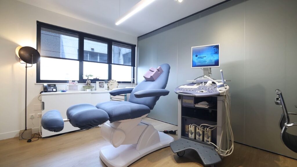 Moderner Ultraschallraum in einer Kinderwunschklinik mit medizinischem Ultraschallgerät und Anatomietafeln des weiblichen Reproduktionssystems an der Wand.